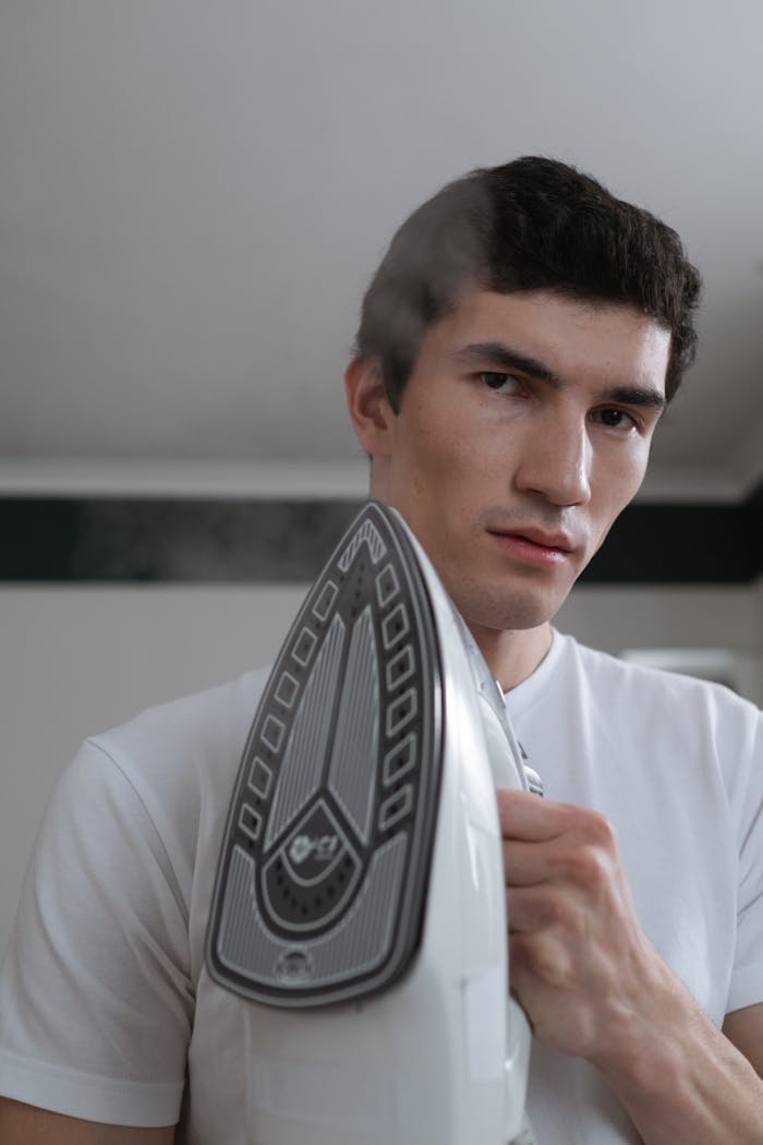 A man holding a steam iron indoors, focusing on household chores.